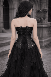 Woman wearing a black gothic-style dress with a corset back in an outdoor setting.